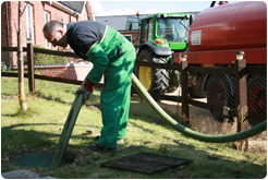 Emptying a septic tank by hose, with the green tractor and red tanker behind